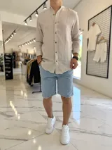 Camisa de lino a rayas beige y blancas, con cuello mao y cierre frontal de botones marrones, de manga larga.