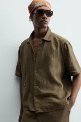 Camisa de corte relajado confeccionada en lino color verde militar, con cuello solapa, manga corta y cierre frontal de botones.