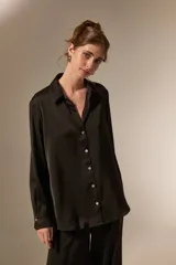 Camisa de poliéster con acabado satinado, de corte holgado, cuello camisero clásico, cierre frontal con botones y mangas largas con puños.