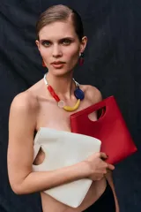 Bolso de mano de piel color rojo, con diseño de cuerpo asimétrico y asa de mano integrada con apertura lateral. Incluye correa bandolera extraíble y bolsillo interior.