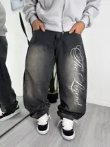 Pantalón de jean estilo baggy, color negro con efecto lavado desgastado. Presenta un diseño amplio y holgado con una estampa tipográfica grande en color blanco en la pierna izquierda.