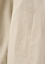 Chaqueta crop estilo gabardina corta color beige, de diseño recto, cuello alto tipo embudo, manga larga, bolsillos laterales y cierre cruzado de doble botonadura con botones oscuros. Con forro interior de poliéster.