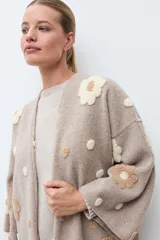 Sacón abierto de tejido de punto en color tostado, con diseño de flores en relieve aplicadas en tonos crema y beige. Presenta mangas largas y corte holgado.