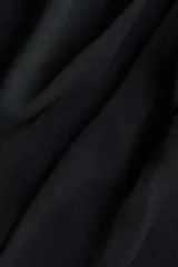 Vestido corto negro con leve brillo, sin mangas, escote bote y detalles de tiras para atar en un hombro y en la cintura con fruncidos laterales.
