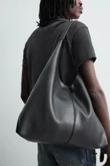 Bolso shopper negro de hombro, de diseño liso y estructura suave, con compartimento principal y asa integrada.