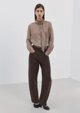 Blusa de manga larga con estampado de rayas verticales en tonos marrones y crema. Presenta un cuello alto con una corbata integrada del mismo tejido y cierre frontal de botones ocultos.
