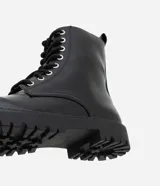 Bota estilo coturno de caña media, confeccionada en poliuretano con acabado liso. Presenta cierre mediante cordones frontales con ojalillos metálicos y suela track robusta.