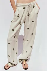 Pantalón color crema de tiro medio con cintura elástica ajustable y bolsillos delanteros. Presenta bordados florales en negro y corte ancho.