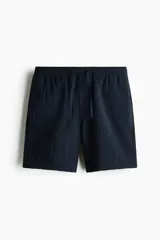 Pantalon corto de corte relajado color azul marino, confeccionado en tejido texturizado suave de mezcla de viscosa. Cuenta con cierre decorativo, cintura con elástico revestido y cordón de ajuste, bolsillos laterales discretos y bolsillo trasero insertado.