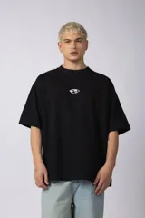 Remera negra de corte oversize con cuello redondo y estampa pequeña en el centro del pecho con forma de ojo que contiene un símbolo de yin y yang.