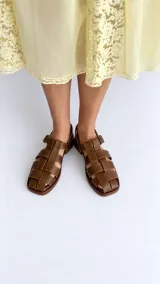 Sandalias de cuero color marrón, estilo romano con tiras entrelazadas, punta cuadrada y cierre de hebilla metálica en el tobillo.