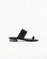 Sandalia plana de cuero color negro, con una tira ancha superior con textura, tira separadora de dedo con detalle metálico y suela con tachas doradas decorativas.