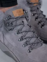 Botas de estilo montañés color gris, confeccionadas en cuero y poliéster. Presentan cuello con forro de piel sintética, ajuste mediante cordones con ganchos metálicos y suela de goma con tecnología Spinal Flex para mayor confort.