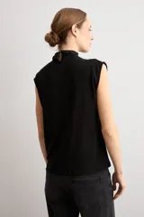 Blusa de lurex negra sin mangas, con cuello alto drapeado y detalle de pliegues frontales.