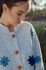 Cardigan de lana color celeste con cuello redondo, cierre frontal con botones color naranja y flores bordadas en azul y celeste.
