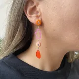 Aros colgantes con pasador y avíos metálicos plateados. Presentan un círculo naranja, una figura abstracta transparente con borde rosa, un círculo rosa con un strass y una pieza colgante naranja.