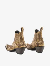 Bota corta estilo texana/cowboy de cuero con acabado metálico dorado envejecido y detalles de grabado en la puntera y el lateral. Posee elásticos laterales y un tacón ancho y bajo.