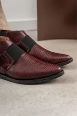 Zapato tipo botineta de cuero color bordó con textura grabada, diseño de punta fina y detalles de elásticos laterales en color negro.