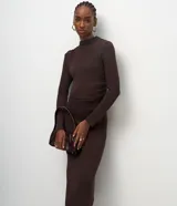 Vestido midi de punto color marrón chocolate, con manga larga, cuello alto sutil y detalle de fruncido lateral que ajusta la silueta. Diseño minimalista de corte recto.