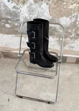 Botas de caña alta confeccionadas en ecocuero negro, con diseño de tres hebillas metálicas laterales y suela plana.
