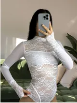 Body de encaje blanco con cuello alto y mangas largas de microtul. Presenta un diseño entallado con detalles de puntilla en los puños y en el borde inferior, combinando transparencias y texturas delicadas.