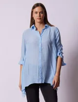 Camisa larga de rayón, con cuello clásico, cierre frontal con botones y mangas regulables con presilla. Presenta un diseño holgado con tajos laterales en el ruedo.