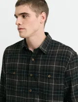Camisa de franela a cuadros con cuello button-down, manga larga y botones de madera. Presenta dos bolsillos tipo parche en el frente con cierre de botón.