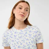 Vestido corto blanco con delicado estampado de pequeñas flores azules, de manga corta y cuello redondo. Presenta un diseño ajustado con un nudo decorativo fruncido en el lateral de la cintura.