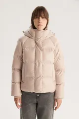 Campera puffer corta color beige con capucha desmontable, cierre frontal con cremallera y botones a presión, y cordón ajustable en el ruedo. Diseño acolchado con bolsillos laterales.