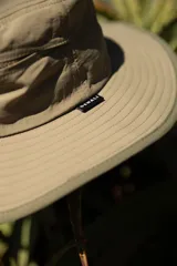 Sombrero tipo pescador color beige con ala ancha, borde reforzado, correa ajustable y parche frontal con el logo de Denali.