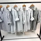 Camisa de manga larga a rayas verticales en tonos grises, con cuello italiano y logo bordado en el pecho.