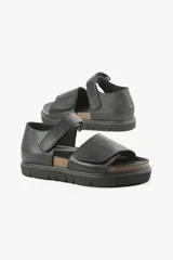 Sandalia plana negra de cuero, con tiras anchas cruzadas y ajuste con velcro.