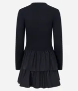 Vestido corto negro de viscosa con mangas largas, cuello redondo y falda godê con superposición de volantes. La parte superior es acanalada y la inferior tiene capas fruncidas.