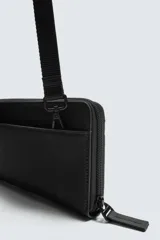Cartera tipo bandolera o billetera con correa ajustable, color negro, con acabado engomado y cierres de cremallera.