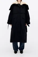 Gabardina larga acolchada color negro con cuello de piel sintética color crema, chaleco interior desmontable con cierre de cremallera, cierre frontal con botones, mangas largas con lazos en los puños y logo bordado en el pecho.