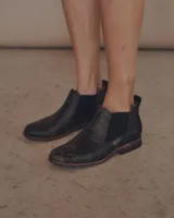 Botines Chelsea de cuero negro con elástico lateral y suela marrón.