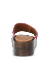 Sandalia tipo slide con capellada de gamuza en color fucsia, con plataforma de poliuretano efecto madera y plantilla de cuero marrón.