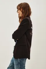 Saco sastre de color negro con corte clásico y solapas. Presenta un bordado artístico en la espalda con motivos de montañas, nubes y flores en tonos suaves.