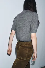 Chaqueta de punto con textura cepillada, cuello polo y manga corta. Presenta cierre frontal con botones y diseño de corte recto.