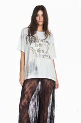 Camiseta de algodón en tono gris claro con efecto desgastado y lavado. Presenta un diseño gráfico frontal con la frase 'If it's meant to be then it will be' y una ilustración de un castillo, con detalles en pedrería o glitter. Posee un corte relajado y mangas cortas.