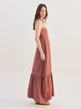 Vestido largo morado de corte suelto, confeccionado en algodón denim, con tirantes ajustables mediante lazos en los hombros y detalle de volado fruncido en el bajo.
