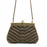 Bolso de mano tipo sobre con diseño vintage, bordado artesanalmente con mostacillas en tonos dorado y negro formando un patrón de líneas en zigzag. Cuenta con una boquilla metálica dorada con detalles florales grabados y una cadena fina a tono para llevar al hombro.