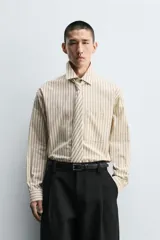 Camisa de corte relajado confeccionada en algodón, con estampado de rayas verticales. Presenta cuello solapa, manga larga con puños abotonados, bolsillo frontal y corbata integrada del mismo tejido.