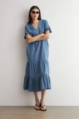 Vestido midi de jean azul, de corte holgado y diseño en capas con volados, escote en V, mangas cortas con detalles bordados en los puños.