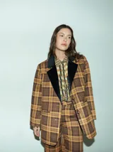 Blazer de corte oversize con estampado de cuadros en tonos marrones y ocres. Presenta solapas de terciopelo negro, cierre frontal con dos botones y bolsillos delanteros. El interior está forrado en satén.