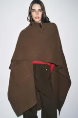 Capa de punto color marrón, con escote en V, mangas cortas y bolsillos de plastrón en el delantero. El ruedo tiene un corte asimétrico.