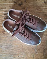 Zapatilla urbana de cuero con diseño combinado en color dorado metalizado y gamuza en tono tostado. Presenta cordones al tono, suela de goma blanca y detalles en cuero marrón en la parte posterior.