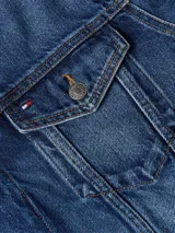 Campera Tommy Hilfiger de denim azul, corte clásico, con cuello inglés, cierre de botones, dos bolsillos tipo sobre con botón en el pecho, dos bolsillos laterales de ojal, puños con botón y logo de Tommy Hilfiger bordado en el pecho.