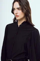 Camisa blanca de manga larga abullonada, con cuello alto y volados delicados en el borde.