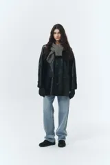 Chaqueta larga de cuero sintético color negro, de silueta amplia y estilo masculino. Presenta cierre frontal con botones, bolsillos delanteros con solapa y forro interior.